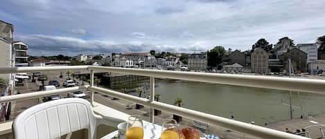 A balcony with a table set for breakfast, overlooking a river and cityscape.
