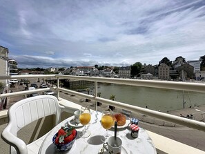 En balkong med ett bord dukat för frukost, med utsikt över en flod och stadens silhuett.