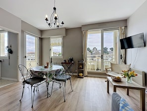 Un soggiorno moderno con zona pranzo, ampie finestre, televisore a schermo piatto e lampadario.
