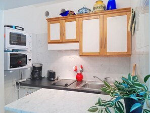 A kitchen with wooden cabinets, a microwave, a toaster, a coffee maker, and a sink. - Le Grand Large by Interhome (Cagnes-sur-Mer)