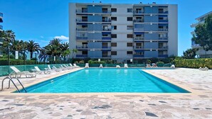 A swimming pool with lounge chairs, a tiled deck, and a multi-story building in the background. - Le Grand Large by Interhome (Cagnes-sur-Mer)