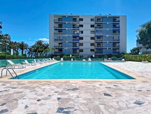 A swimming pool with lounge chairs, a tiled deck, and a multi-story building in the background. - Le Grand Large by Interhome (Cagnes-sur-Mer)
