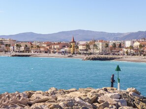 A coastal town with a rocky shoreline, a lighthouse, and a mountain range in the background. - Le Grand Large by Interhome (Cagnes-sur-Mer)