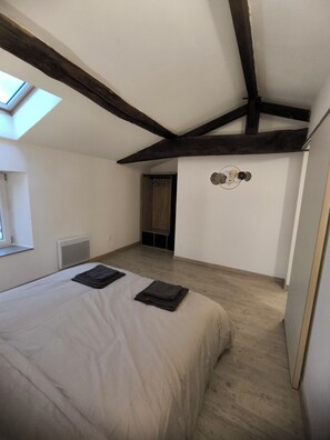A bedroom with a sloped ceiling, a bed, a radiator, and a small window. - T2 apartment for 2 to 4 people (Les Epesses)