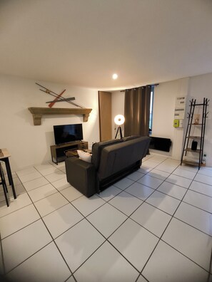 A modern living room with a sofa, TV, and a lamp. - T2 apartment for 2 to 4 people (Les Epesses)