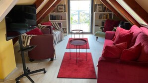 Et kvistværelse med skråvæg, en rød sofa, en stribet lænestol, et lille bord og en reol.