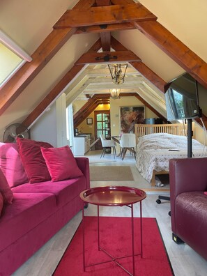 An attic bedroom with a bed, a TV, a red carpet, and a pink sofa.