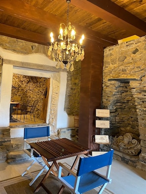 A rustic interior with a stone wall, a wooden ceiling, and a chandelier. There is a table with blue chairs and a sign with text.