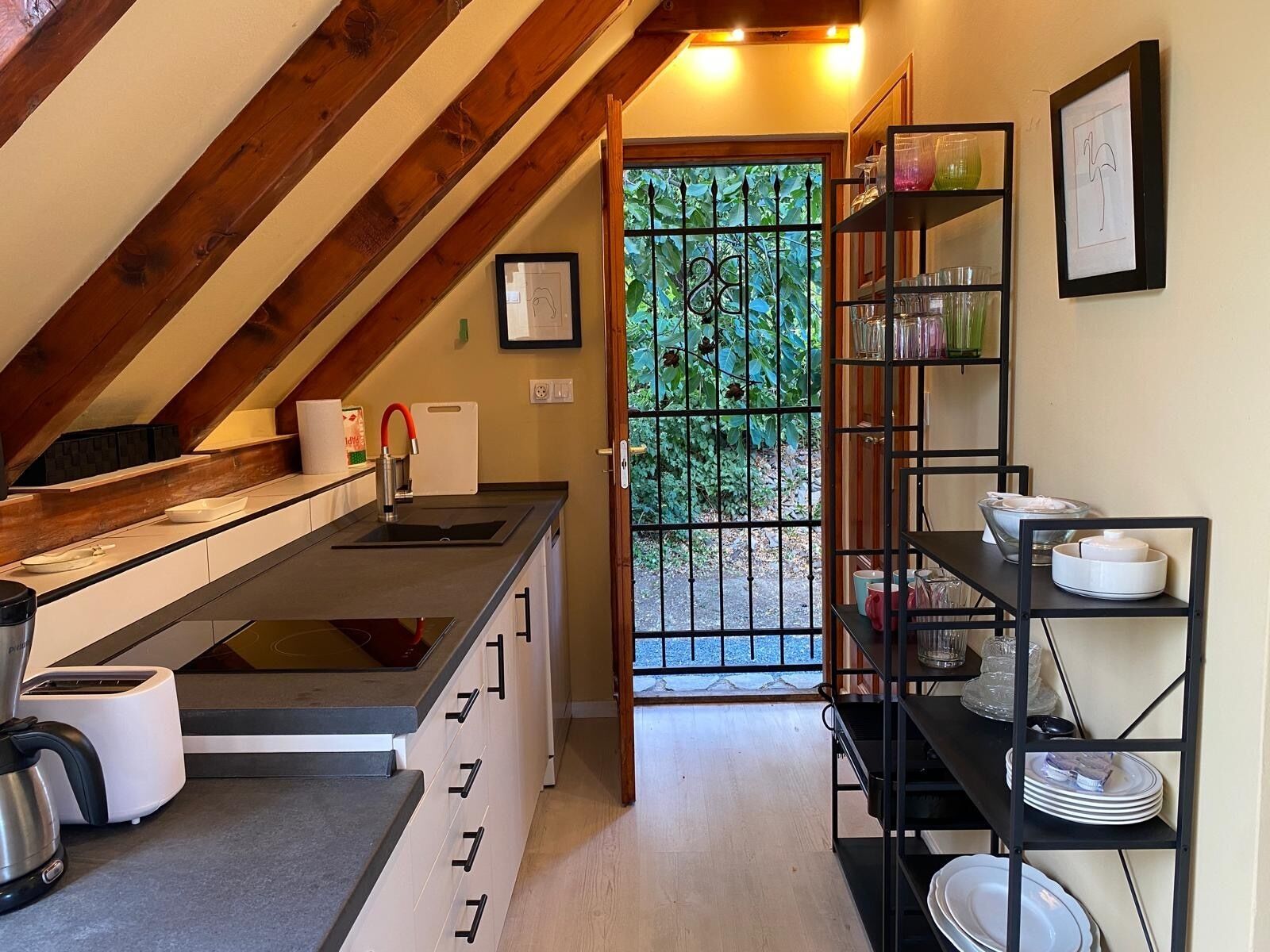 Una cocina compacta con horno integrado, un lavabo y una zona de comedor con estantería de metal negro.