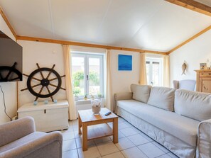 Ein Wohnzimmer mit einer Couch, einem Holztisch, einem Fernseher, einer Schiffslenken-Dekoration und einem Fenster mit Vorhängen.