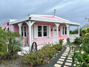 Una casa rosa e bianca con un portico, circondata da piante e un vialetto in pietra.