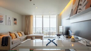 Un salon moderne avec un canapé, une table basse en verre, un téléviseur et une vue sur le balcon.