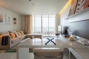 Ein modernes Wohnzimmer mit einer Couch, einem Glastisch, einem Fernseher und Blick auf einen Balkon.
