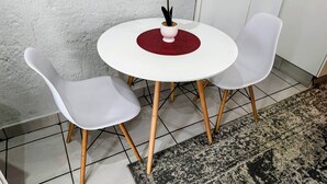 A round white table with two white chairs, a red placemat, and a white vase with white flowers.