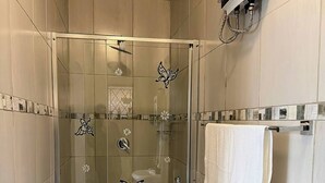 A glass-enclosed shower with a tiled floor, a white towel on a rack, and a wall-mounted air conditioning unit.