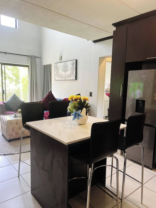A modern kitchen with a central island, black chairs, a refrigerator, and a dining table. - Zalari Luxe Loft B, Nature 1-bed Loft, Paulshof (Johannesburg)
