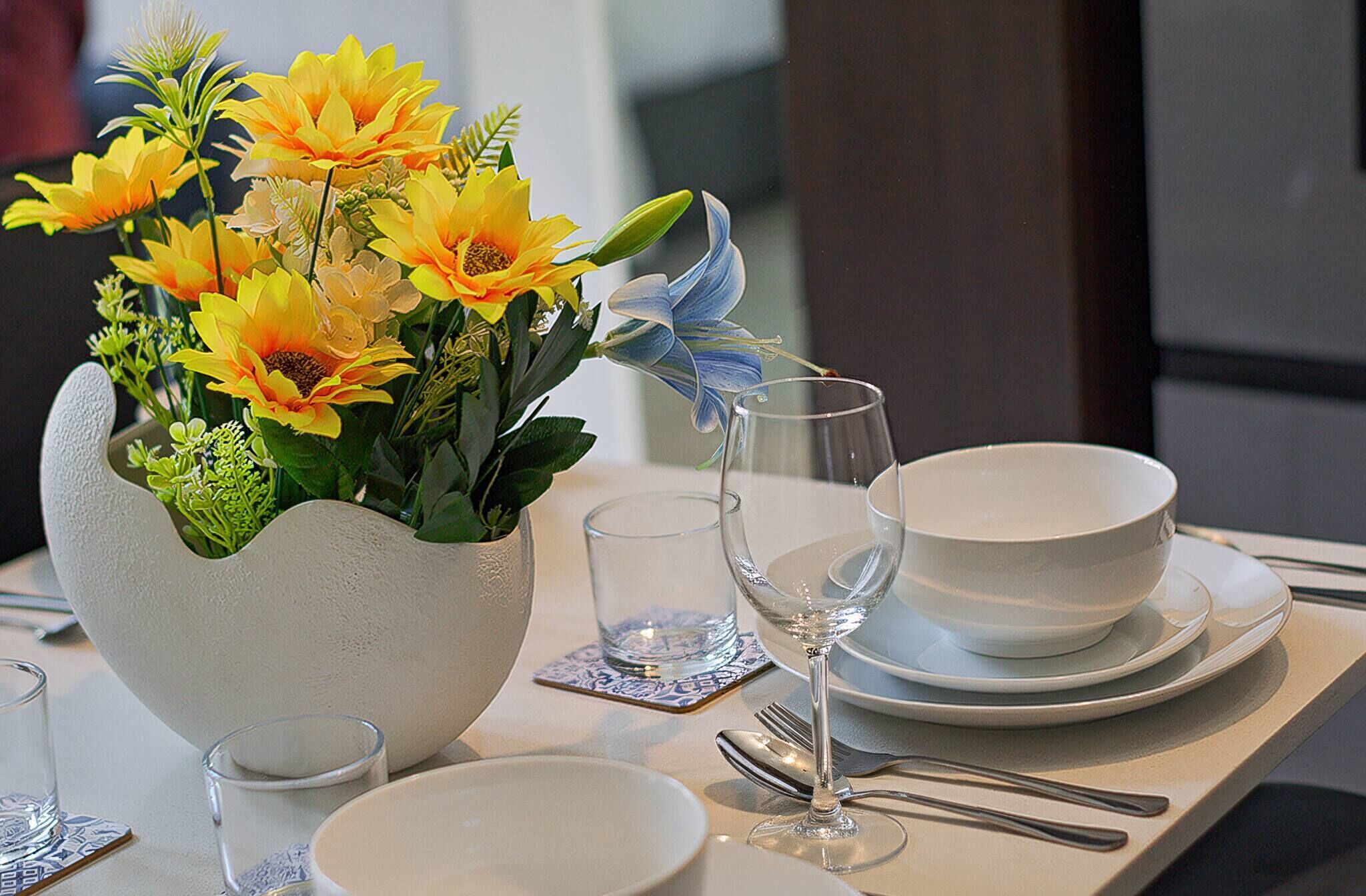 A table set with a white vase of yellow flowers, clear glasses, a wine glass, and white plates.