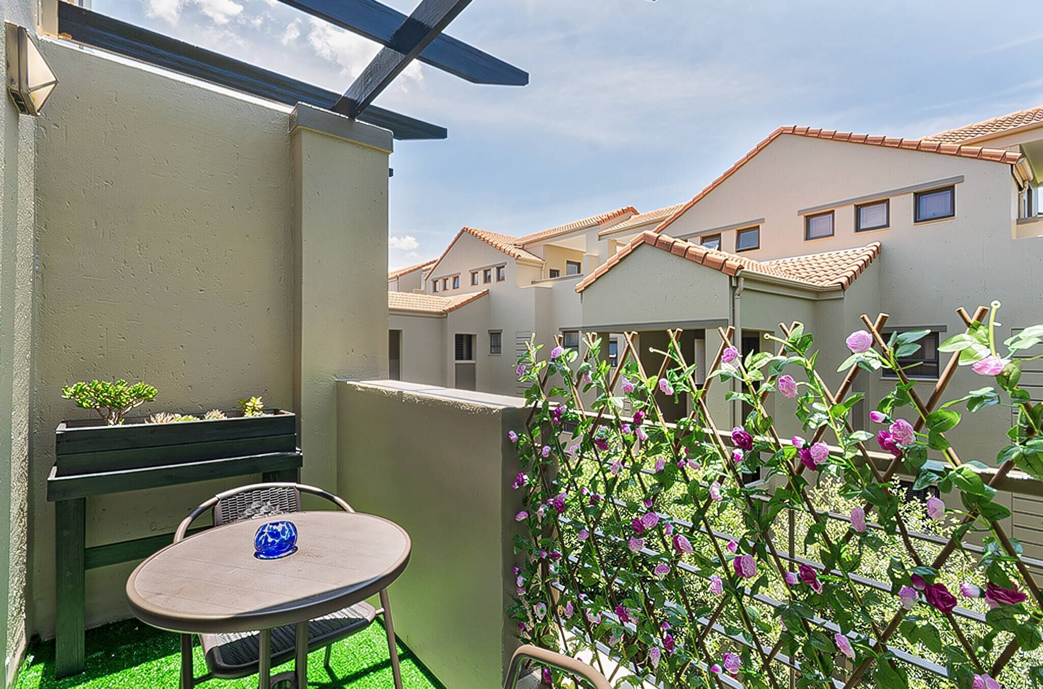 A balcony with a table and chairs, a small plant, and a trellis with flowers.