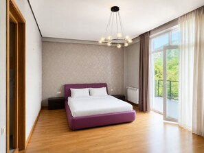 Un dormitorio moderno con una cama grande, una mesita de noche, un aparador y vistas a zonas verdes a través de un ventanal amplio.
