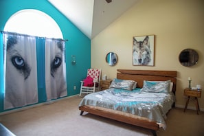 Ein Schlafzimmer mit einem Bett, einem Sessel, einem Nachttisch, einem Spiegel und einem Bild von einem Wolf.