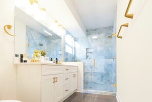 Ein modernes Badezimmer mit einem großen Spiegel, weißen Schränken, einer Dusche mit Glastüren und goldenen Armaturen.