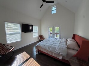 Un dormitorio con cama, televisor, ventilador de techo y ventana.