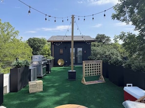 Ein Garten mit Kunstgrashalm, einem Grill, einem Ventilator und einem hölzernen Spielbrett.