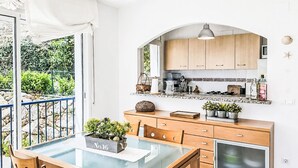A modern kitchen with wooden cabinets, a glass dining table, and a view of the garden. - El Jardinet by Interhome (Llançà)