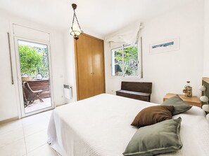 Une chambre à coucher comprenant un lit, une armoire en bois, un banc, une fenêtre donnant sur un paysage verdoyant et une table de chevet avec une lampe.