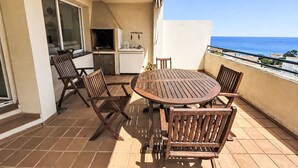 A patio with a round wooden table and four chairs, a small kitchen area, and a view of the ocean. - El Jardinet by Interhome (Llançà)
