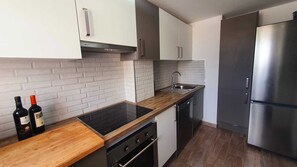 Eine moderne Küche mit weißen Schränken, einem Edelstahlkühlschrank, einer schwarzen Induktionskochplatte und einer Holz Arbeitsplatte.