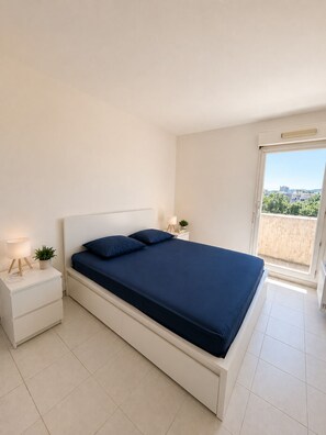 Ein Schlafzimmer mit einem Bett, zwei Nachttischen, einem Fenster und Blick auf die Stadt.