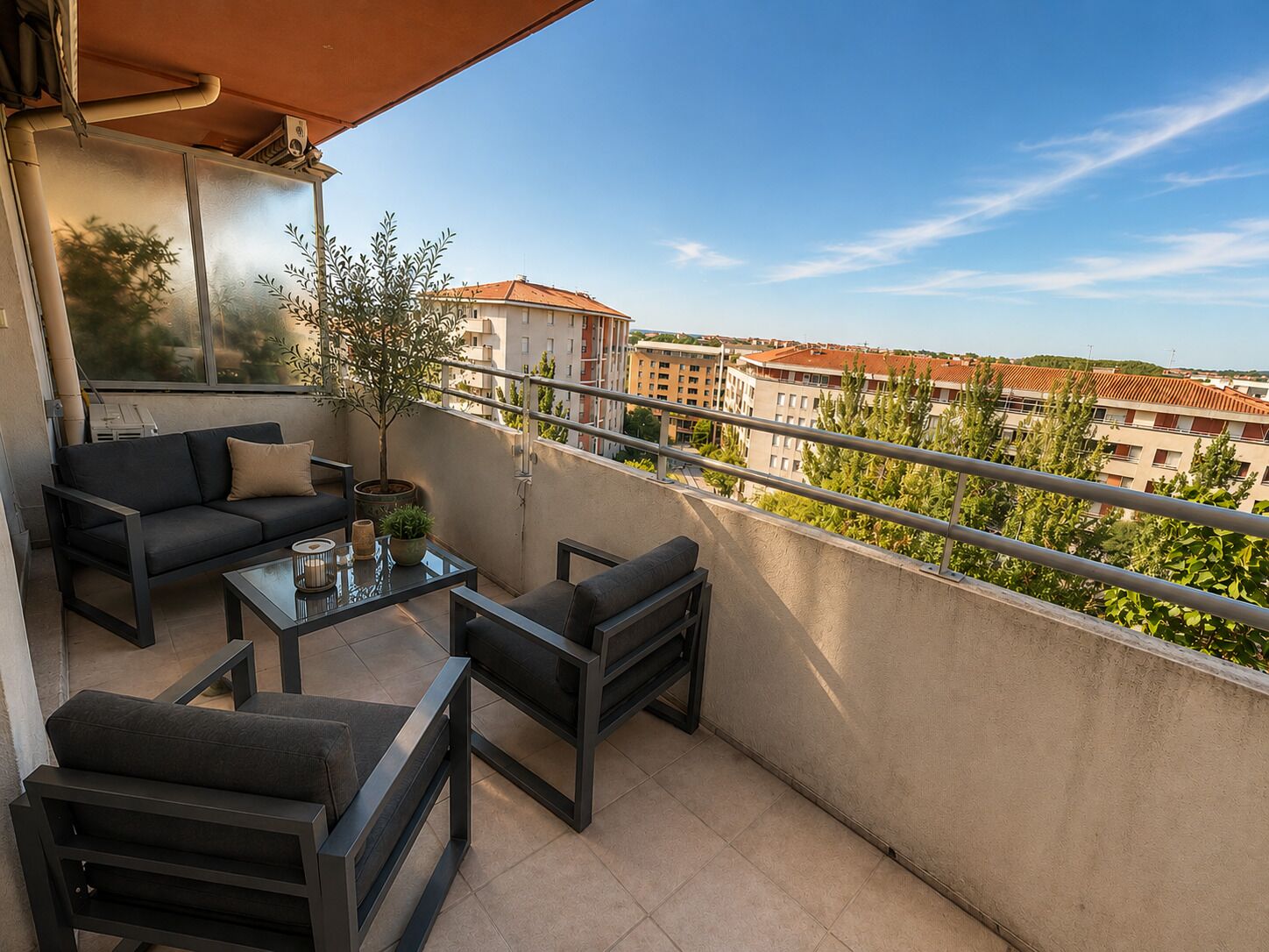 A balcony with a sofa, chairs, a table, and a potted plant.