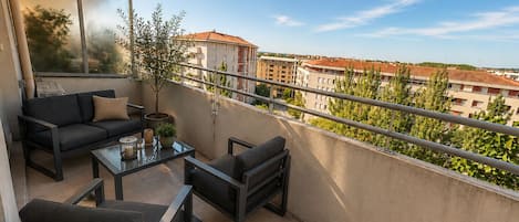 A balcony with a sofa, chairs, a table, and a potted plant.