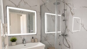 Et moderne badeværelse med en glasbrusekabine, et hvidt toiletbord med et spejl og vægge med marmorlook.