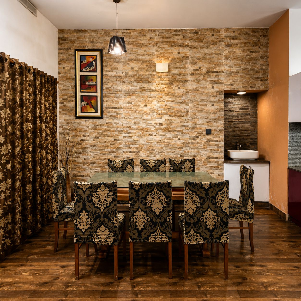 Un coin repas avec une table en verre et des chaises à motifs, un mur en pierre et un espace cuisine équipé d’un évier.