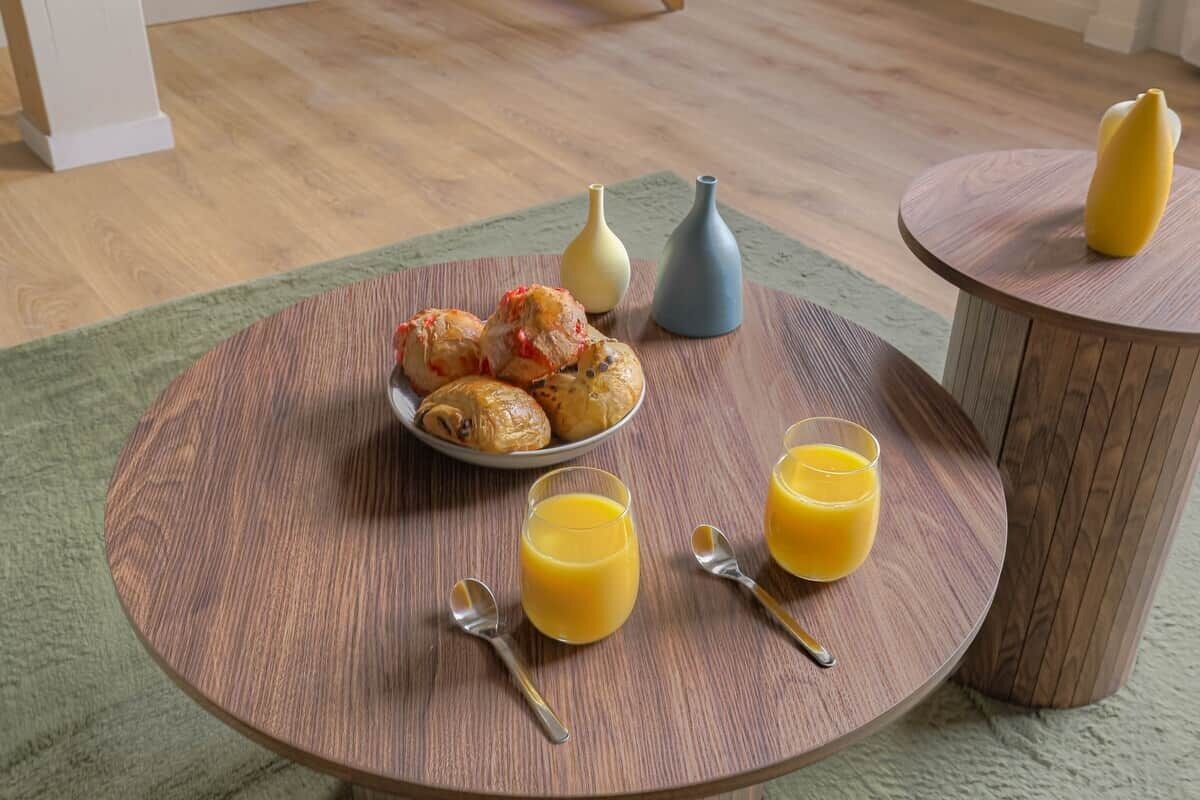 A round wooden table with a plate of pastries, two glasses of orange juice, and two spoons.