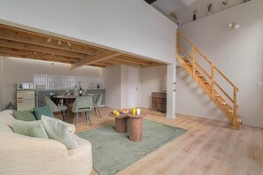 Un vaste espace de vie agrémenté d’un escalier en bois, d’une table à manger avec des chaises, et d’une cuisine située au fond de la pièce.