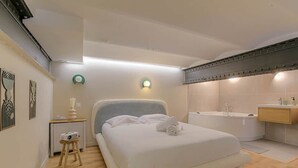 Een slaapkamer met een bed, nachtkastje, lamp en een badkamer met bad en wastafel.