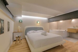 Une chambre à coucher comprenant un lit, une table de chevet et une lampe, ainsi qu’une salle de bain avec une baignoire et un lavabo.