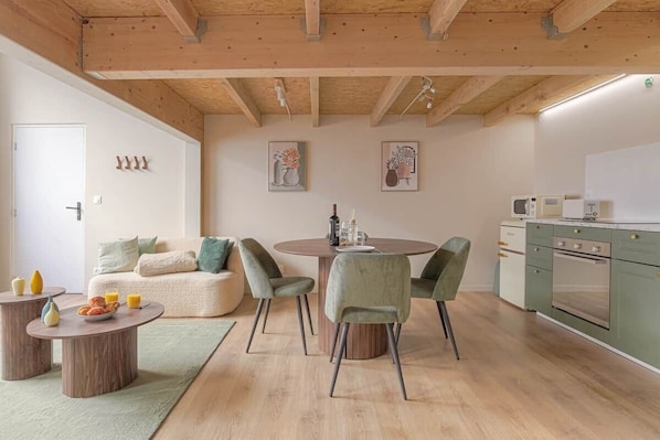 Une cuisine moderne avec des poutres en bois, un coin repas avec une table ronde et des chaises, et un coin cuisine équipé d’un four à micro-ondes et d’un four traditionnel.