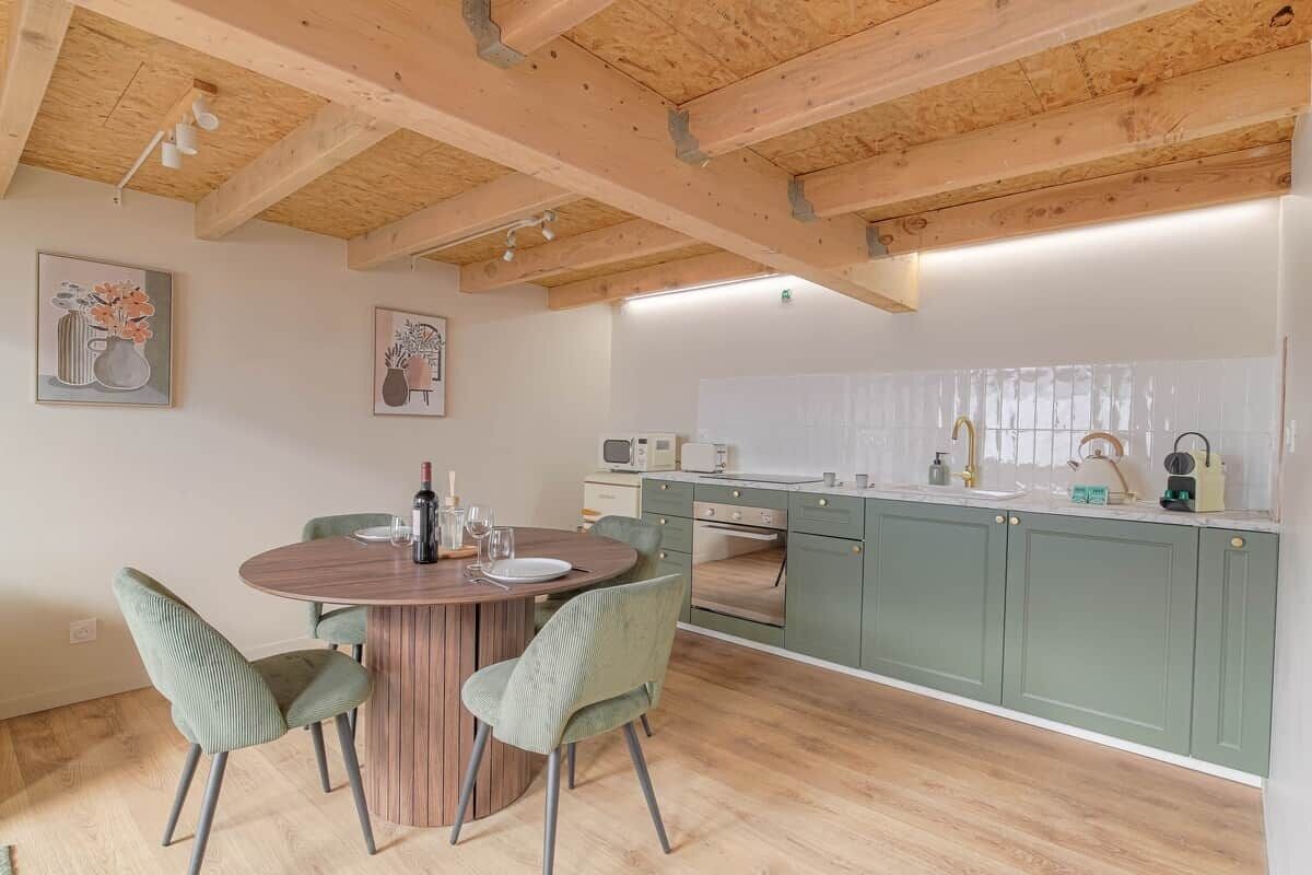 A kitchen with wooden beams, green cabinets, a round dining table, and two chairs.