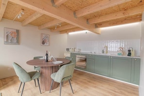 Une cuisine avec des poutres en bois, des meubles de couleur verte, une table de salle à manger ronde et deux chaises.