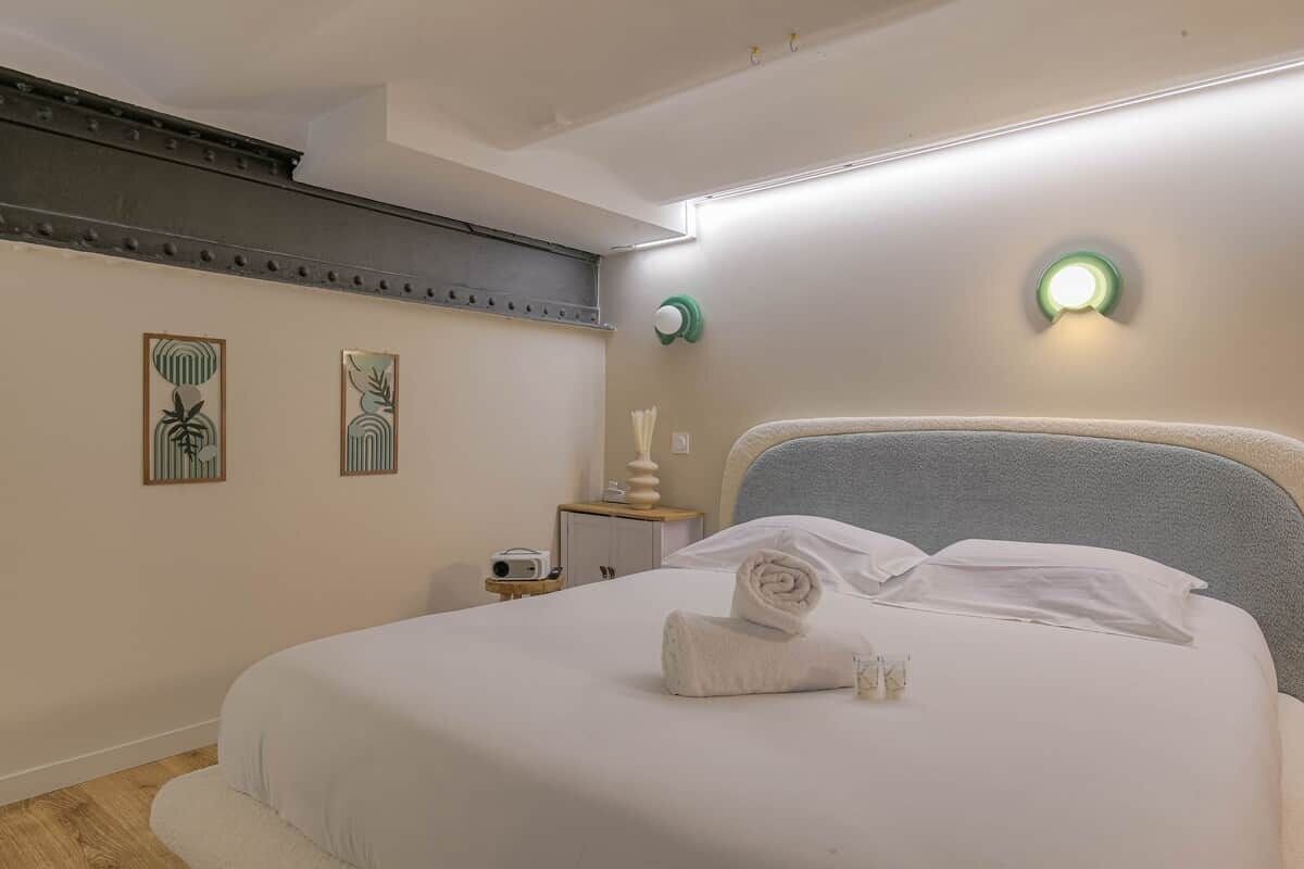 A neatly made bed with a rolled towel, a bedside table with a lamp, and two wall-mounted light fixtures.