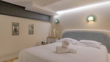 A neatly made bed with a rolled towel, a bedside table with a lamp, and two wall-mounted light fixtures.