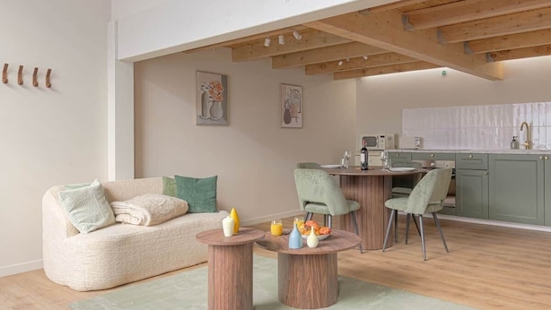 Een moderne woonkamer met een bank, twee bijzettafels en een eethoek met stoelen.