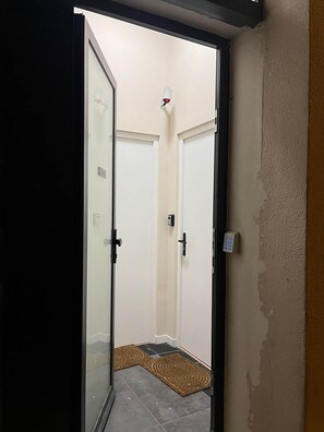 Une porte qui donne sur une pièce avec une porte blanche, un petit tapis sur le sol et un luminaire fixé au mur.