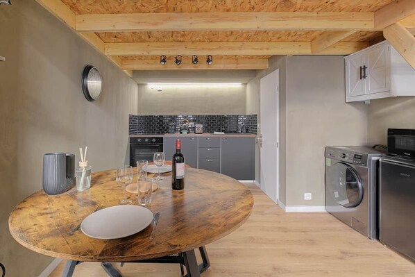 Una cocina con una mesa redonda de madera dispuesta para comer, una lavadora y un microondas.