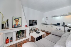 Ein modernes Wohnzimmer mit Kamin, Flachbildfernseher, einer Couch und einer Küchenzeile mit weißen Schränken und einer Waschmaschine.