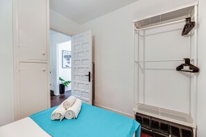 Ein Hotelzimmer mit einem Bett, einem weißen Kleiderschrank, einer Tür zu einem anderen Raum und einem an der Wand befestigten Wäscheständer.